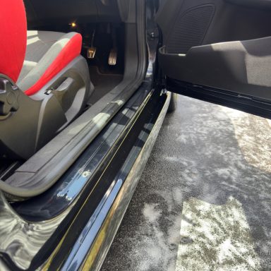 View of a car's interior showing a red seat and the open door with the threshold visible.