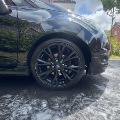 Black car with large black alloy wheels parked on a driveway.