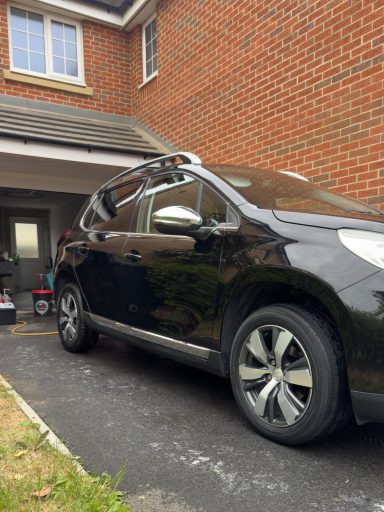Black car parked in front of a brick house with a garage.