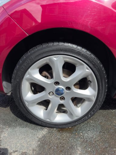Close-up of a silver alloy wheel on a pink car.