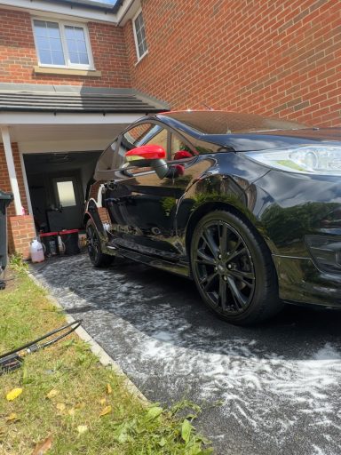 Black car being cleaned on a driveway outside a brick house.