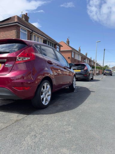 A red car parked on a residential street alongside another vehicle.