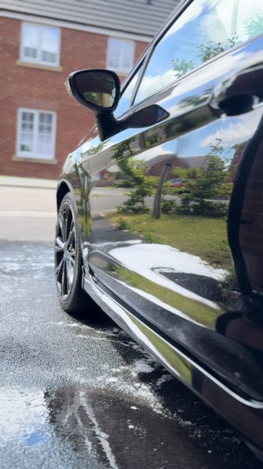 Black car reflecting surroundings, with a focus on the side view mirror and clean surface.