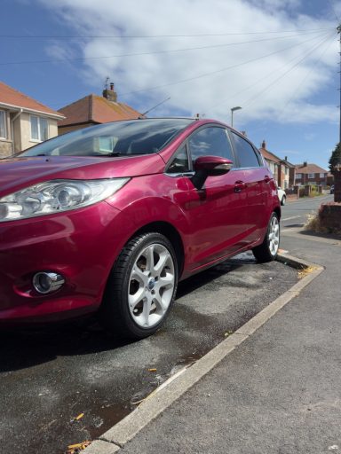 A red car parked beside a residential street under a clear blue sky.